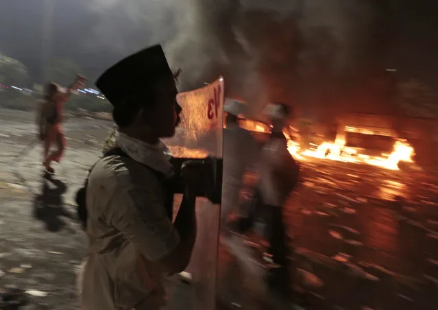 A Muslim youth carries a riot shield near burning police trucks, during a clash with the police outside the presidential palace in Jakarta, Indonesia, Friday, November 4, 2016. (Photo by Dita Alangkara/AP Photo)