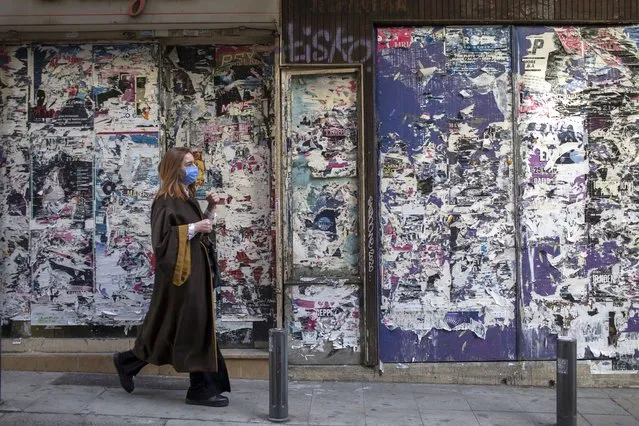 A woman wearing a face mask to curb the spread of the coronavirus walks outside shuttered shops on Tuesday, February 9, 2021. Authorities in Greece have extended a curfew in the country's two largest cities after a new rise in COVID-19 cases. (Photo by Petros Giannakouris/AP Photo)