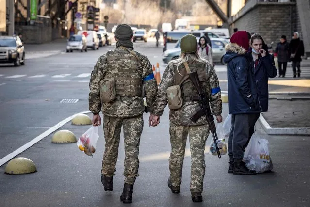 A couple of Ukraine soldiers holds hands as they walk in the street in Kyiv, on March 18, 2022. Authorities in Kyiv said one person was killed early on March 18, 2022 when a downed Russian rocket struck a residential building in the capital's northern suburbs. They said a school and playground were also hit. (Photo by Fadel Senna/AFP Photo)