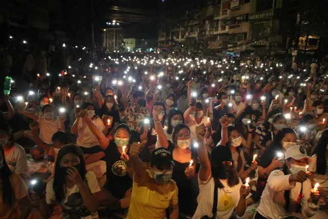People raise their hands with clenched fists while others hold up mobile phones with LED lights on, during a candlelight night rally in Yangon, Myanmar Saturday, March 13, 2021. (Photo by AP Photo/Stringer)