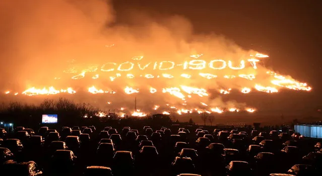 Spectators sitting inside their vehicles enjoy the Jeju Fire Festival as the fire forms the letters “COVID-19 OUT” at a hill in Jeju, South Korea, March 13, 2021. (Photo by Yonhap via Reuters)