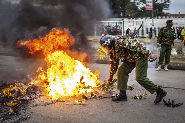A police officer tries to put out a burning barricade erected by demonstrators during protests in the capital Nairobi, Kenya Friday, July 7, 2023. Dozens of anti-government protesters were arrested in Nairobi on Friday as other parts of the country also witnessed demonstrations called by the opposition against newly imposed taxes and the cost of living. (Photo by Samson Otieno/AP Photo)