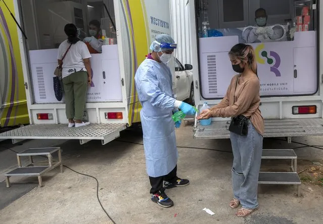 A health worker sprays disinfectant on hands after collecting a nasal swab from worker in a local entertainment venue area where a new cluster of COVID-19 infections were found in Bangkok, Thailand, Thursday, April 8, 2021. Thailand has confirmed its first local cases of the coronavirus variant first detected in the U.K., raising the likelihood that it is facing a new wave of the pandemic, a senior doctor said Wednesday. (Photo by Sakchai Lalit/AP Photo)