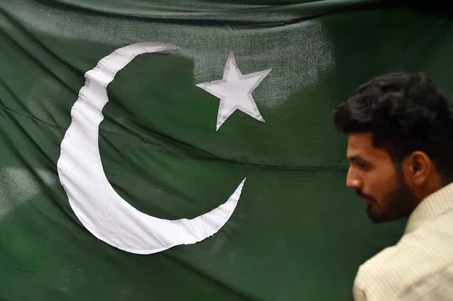 A man stands in front of a Pakistani national flag at a market where vendors are selling decorative masks and items with the colors of the national flag ahead of Independence Day celebrations in Karachi, Pakistan, 13 August 2023. (Photo by Shahzaib Akber/EPA/EFE)