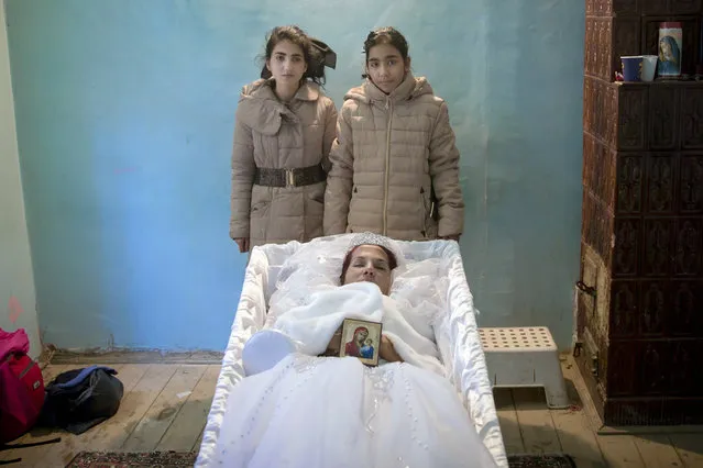 In this Tuesday, November 3, 2015 photograph, Maria Ion, a 38 year-old widow, mother of five, who died in last Friday's fire at the Colectiv nightclub where she occasionally worked as a cleaning lady, lies in a coffin wearing a bride dress as two of her children, Denisa, 15 years-old, left, and 11 year-old Alexandra pose next to it, at the family house in Bucharest, Romania. The Oscar-nominated Romanian documentary film “Collective” follows a group of journalists delving into the state of health care in the eastern European country in the wake of a deadly 2015 nightclub fire that left dozens of burned victims in need of complex treatment. What they revealed was decades of deep-rooted corruption, a heavily politicized system scarily lacking in care. (Photo by Vadim Ghirda/AP Photo/File)