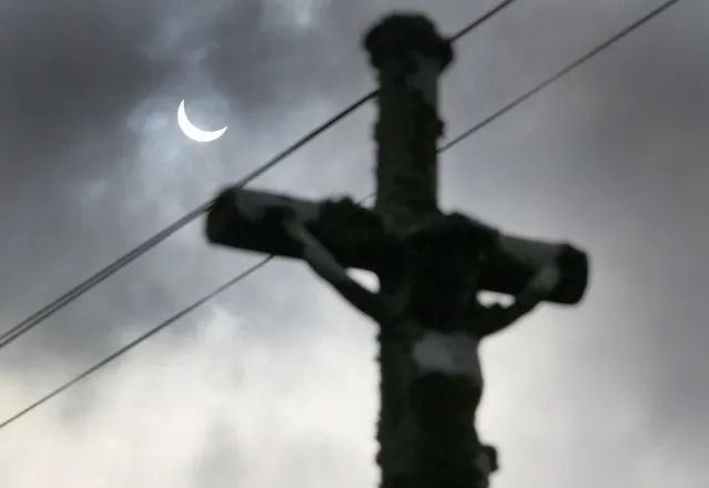 A partial eclipse of the sun is seen through clouds behind a roadside crucifix at Goulien, in Finistere, western France, March 20, 2015. (Photo by Mal Langsdon/Reuters)