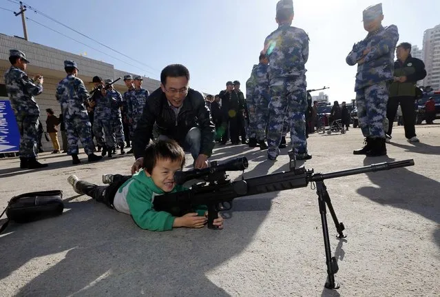 A boy plays with an unloaded gun during a Special Weapons and Tactics (SWAT) open day in Qingdao, Shandong province, November 7, 2013. Nearly 300 residents attended the open day on Thursday to take a closer look at guns, explosive ordnance disposal (EOD) robots and riot police cars displayed in the yard of a SWAT police station of the city. (Photo by Reuters/Stringer)