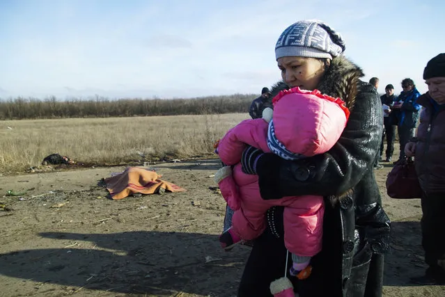 A woman with her child and others pass body of the man, who died in a land mine explosion near a frontline crossing to Ukrainian government controlled territory, in the war conflict-hit Donetsk region, near Donetsk, eastern Ukraine on Wednesday, February 10, 2015. Clashes between Ukrainian government forces and pro-Russia rebels in eastern Ukraine has continued despite a peace deal signed a year ago, and large areas are littered with mines. (Photo by Mstyslav Chernov/AP Photo)