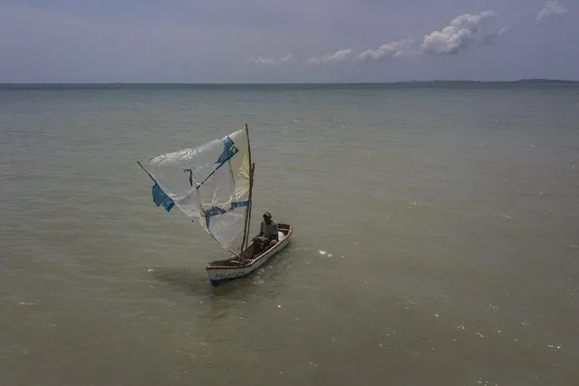 A fisherman navigates his boat with a broken sail made of recycled plastic as he returns to shore in Les Cayes, Haiti, Friday, August 20, 2021, six days after a 7.2 magnitude earthquake hit the area. (Photo by Matias Delacroix/AP Photo)