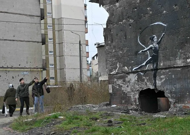 Local residents look at a Banksy-style graffiti on the wall of a destroyed residential building, but its origin remains unconfirmed by the artist, in Irpin, near Kyiv on November 12, 2022, amid the Russian invasion of Ukraine. Banksy, the elusive British street artist, has painted a mural on a bombed-out building outside Ukraine's capital, in what Ukrainians have hailed as a symbol of their country's invincibility. On November 11's night the world-famous graffiti artist posted on Instagram three images of the artwork – a gymnast performing a handstand amid the ruins of a demolished building in the town of Borodyanka northwest of the Ukrainian capital Kyiv. (Photo by Genya Savilov/AFP Photo)