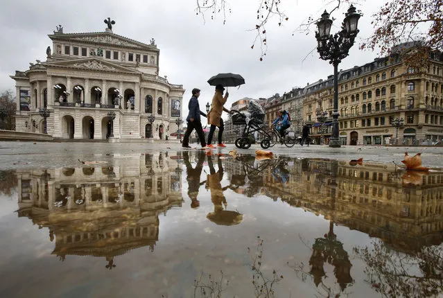 A woman under an umbrella passes by the Old Opera that is reflected in a puddle on a rainy day in Frankfurt, Germany, Wednesday, January 13, 2016. (Photo by Michael Probst/AP Photo)