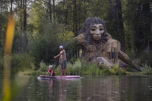 A father and son paddle past “Mama Mimi”, a wooden sculpture created by Danish artist Thomas Dambo in Rendezvous Park on July 26, 2021 in Jackson Hole, Wyoming. Dambo's public art, featuring troll figures are made from recycled and found materials. This troll was completed in June 2021 and joins other public art works made by Dambo throughout the world in places like Puerto Rico, China, Australia, and more. (Photo by Natalie Behring/Getty Images)