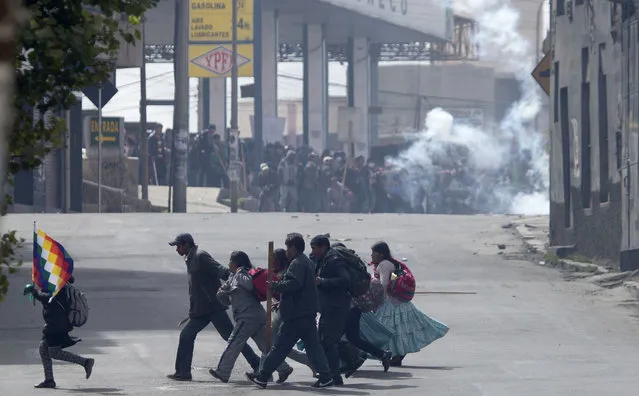 Farmers clash with riot police in the background as another group of demonstrators runs across the street during a protest by coca leaf farmers in La Paz, Bolivia, Tuesday, February 21, 2017. The farmers from a region north of La Paz known as Los Yungas, were dispersed by police with tear gas bombs during a protesting march, after a three-day vigil near the government palace and the National Congress where they had gathered to protest a bill they believe favors coca leaf farmers represented by President Evo Morales. (Photo by Juan Karita/AP Photo)