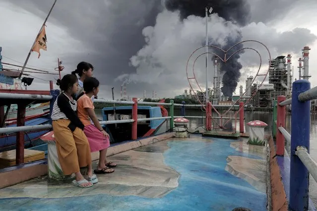 Girls look at black smoke coming from a fire that has broken out at a fuel storage unit at the Pertamina refinery complex in Cilacap, Central Java province, Indonesia on November 14, 2021. (Photo by Idhad Zakaria/Antara Foto via Reuters)
