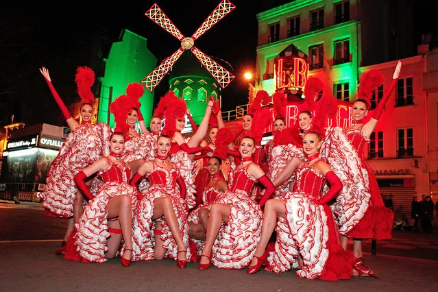 Dancers line up in front of the Moulin Rouge cabaret, in the Montmartre neighbourhood as the exterior is illuminated in green to mark St. Patrick's day, in Paris, Monday, March 17, 2014. (Photo by Thibault Camus/AP Photo)