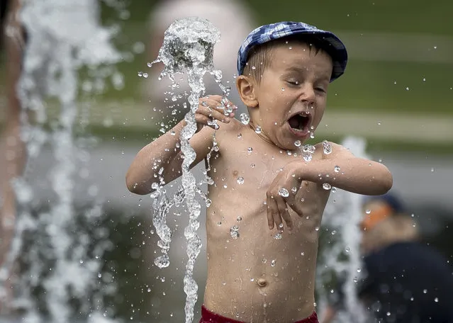 A child plays in water to cool off, at the Lukiskiu square in Vilnius, Lithuania, Wednesday, June 12, 2019. A heat wave continues in the Lithuania as temperature goes up high at 35 degrees Celsius (95 degrees Fahrenheit). (Photo by Mindaugas Kulbis/AP Photo)