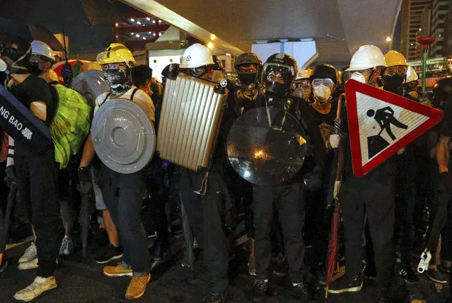 Protesters carrying home-made shields face off with riot policemen on a street in Hong Kong, Sunday, July 21, 2019. Hong Kong police have thrown tear gas canisters at protesters after they refused to disperse. Hundreds of thousands of people took part in a march Sunday to call for direct elections and an independent investigation into police tactics used during earlier pro-democracy demonstrations. Police waved a black warning flag Sunday night before lobbing the canisters into a crowd of protesters. (Photo by Bobby Yip/AP Photo)