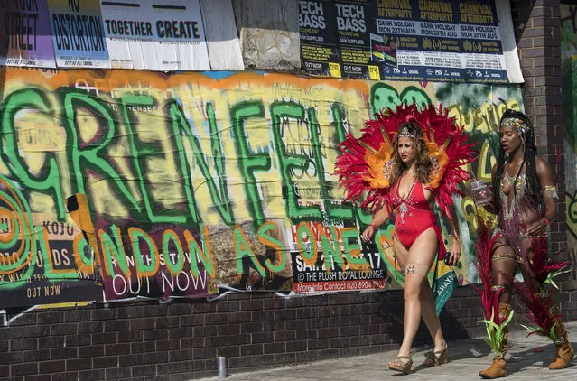 Carnival goers walk past a graffiti sign for Grenfell Tower on the second day of the 2017 Notting Hill carnival in London, England on August 28, 2017. The two day event is the second largest street festival in the world after the Rio Carnival in Brazil, attracting over 1 million people to the streets of West London. (Photo by Ben Cawthra/Rex Features/Shutterstock)
