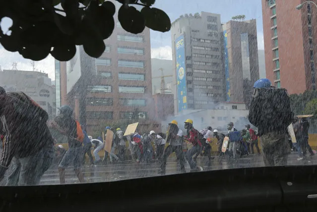 Anti-government protesters shield themselves from sprays of water as security forces try to disperse them, in Caracas, Venezuela, Thursday, May 18, 2017. The protest in Caracas comes after a tumultuous 24 hours of looting and protests in the western state of Tachira that led the government to send in troop reinforcements. More than 40 people have been killed in almost two months of unrest in Venezuela. (Photo by Fernando Llano/AP Photo)