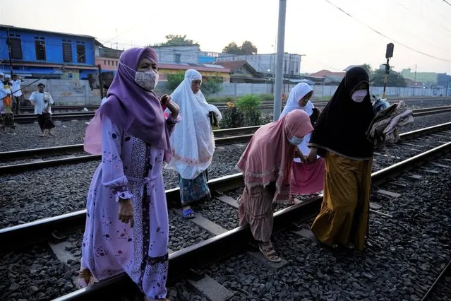 Muslims walk over a railway as they head for an Eid al-Fitr prayer marking the end of the holy fasting month of Ramadan on a street in Bekasi, West Java, Indonesia, Monday, May 2, 2022. (Photo by Achmad Ibrahim/AP Photo)