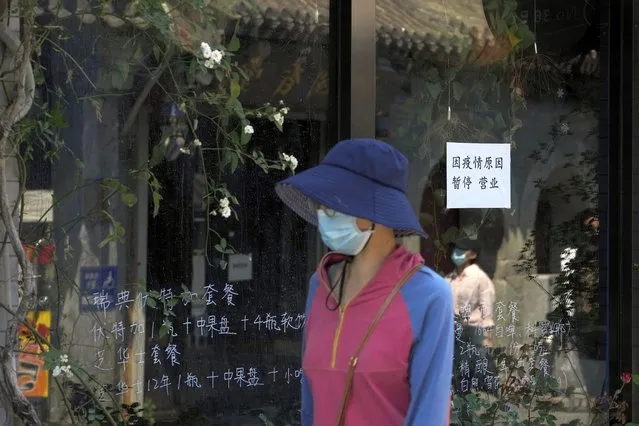 Residents wearing face masks walk by a closure notice on display at a restaurant after authorities ordered the closure of non-essential businesses due to pandemic measures on Monday, May 16, 2022, in Beijing. (Photo by Andy Wong/AP Photo)