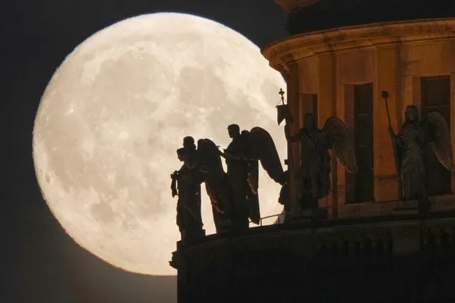 Sculptures of angels fixed at the St. Isaak's Cathedral are silhouetted on the full moon in St. Petersburg, Russia, Monday, June 13, 2022. (Photo by Dmitri Lovetsky/AP Photo)