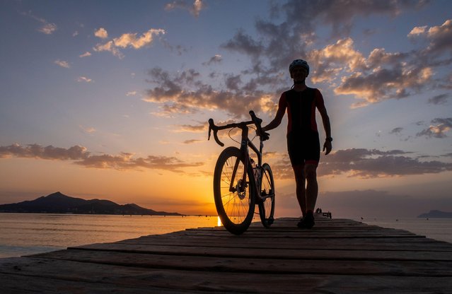 A lovely sunrise in at the beachfront of Playa de Muro, Alcudia on the island of Mallorca, Majorca, Spain on May 16, 2022. As a road cyclist walks his road bike along a wooden jetty heading out into the calm waters. (Photo by Phil Wilkinson/Alamy Live News)