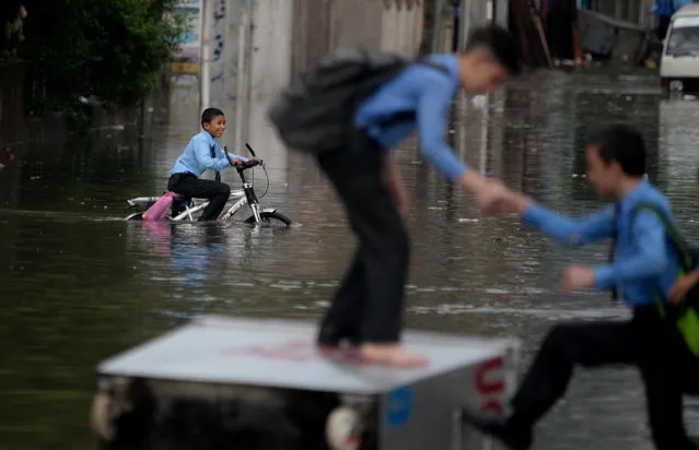 A Pakistani student helps his colleauge to reach on a waste caontainer lying on a flooded street after heavy monsoon rains hit the city of Rawalpindi, Pakistan on August 25, 2017. Heavy monsoon rains flooded streets and submerged hundreds of houses in several low-lying localities causing damages to the houses and the belongings of the residents. (Photo by Muhammad Reza/Anadolu Agency/Getty Images)
