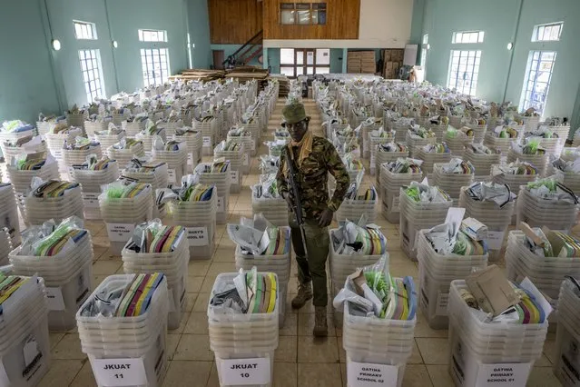 A policeman guards ballot boxes and election materials as they sit ready to be distributed to polling stations, at a counting center in Nairobi, Kenya on Monday, August 8, 2022. Kenya is voting Tuesday in an election that will bring East Africa's economic hub a new president after a decade. (Photo by Ben Curtis/AP Photo)