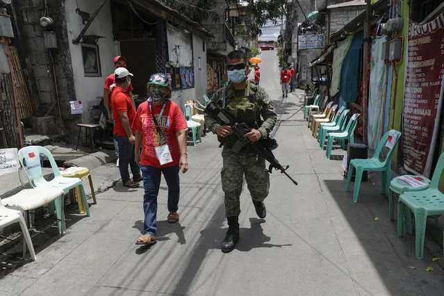 An army soldier walks with a volunteer as they wait for relief goods to be distributed and placed on chairs outside homes during a continuing enhanced community quarantine to prevent the spread of the new coronavirus in Quezon City, Metro Manila, Philippines on Monday, May 4, 2020. (Photo by Aaron Favila/AP Photo)