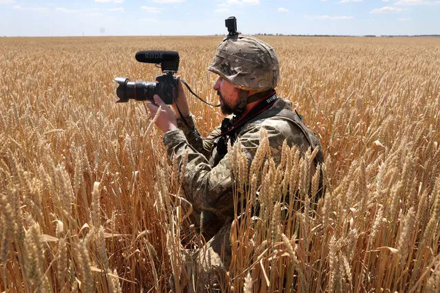 A Ukrainian military journalist takes cover in a wheat field as he captures video while a tank team with the 14th Mechanized Brigade of Prince Roman the Great fire on an enemy position on July 01, 2022 in the Donetsk District, Ukraine. In recent weeks, Russia has concentrated its firepower on Ukraine's Donbas region, where it has long backed two separatist regions at war with the Ukrainian government since 2014. (Photo by Scott Olson/Getty Images)