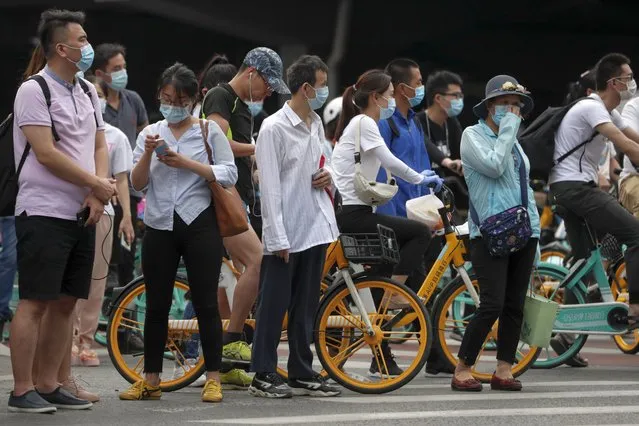 People wearing protective face masks to help curb the spread of the new coronavirus wait to cross a street in Beijing, Monday, June 22, 2020. A Beijing government spokesperson said the city has contained the momentum of a recent coronavirus outbreak that has infected a few hundreds of people, after the number of daily new cases fell to single digits. (Photo by Andy Wong/AP Photo)
