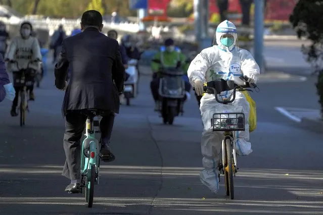 A worker in protective gear rides on a street as she heads to take COVID-19 sample from residents who have been under home quarantine in Beijing, Thursday, November 3, 2022. (Photo by Andy Wong/AP Photo)