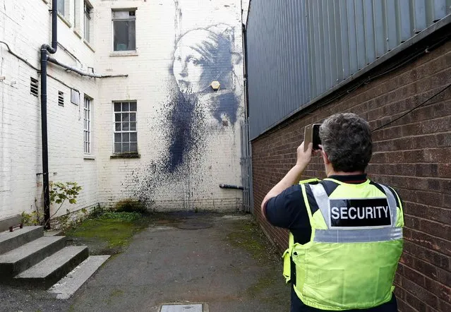 A city council security guard photographs a piece of street art attributed to Banksy titled “The Girl with the Pierced Eardrum” after it was defaced in an alleyway in Bristol, western England, October 22, 2014. (Photo by Andrew Winning/Reuters)