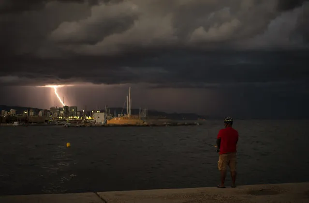 A man is fishing as lightning flashes in the night sky during a storm in Barcelona, Spain on Sunday, August 30, 2020. Spanish authorities have announced new restrictions to prevent COVID-19. (Photo by Emilio Morenatti/AP Photo)