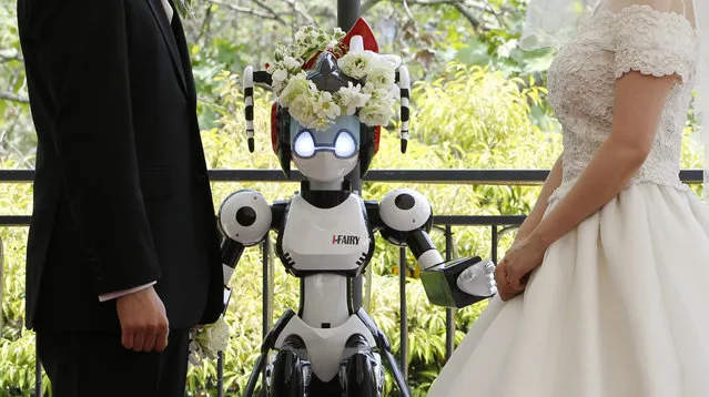 A humanoid robot named “I-Fairy” (C) acts as a witness at the wedding ceremony between Tomohiro Shibata (L) and Satoko Inoue in Tokyo May 16, 2010. The couple decided to use the robot, which conducted the ceremony with its audio functions, from Inoue's company to perform the witness' duties as they first met due to common work interest related to robots. (Photo by Yuriko Nakao/Reuters)