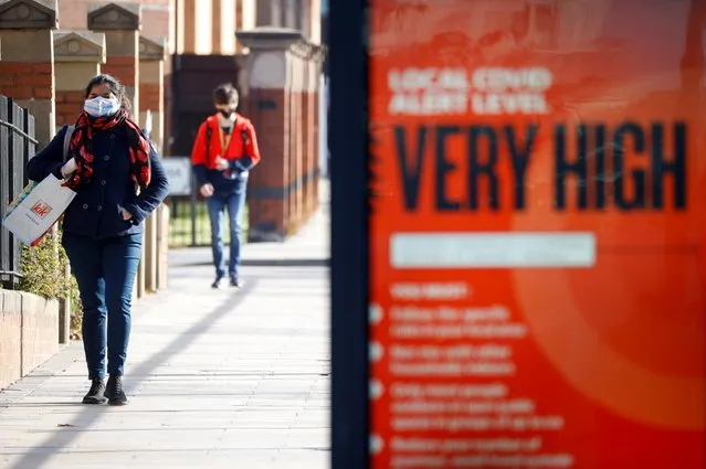 People wearing protective masks walk behind a covid warning sign as the spread of the coronavirus disease (COVID-19) continues, in Liverpool, Britain on October 15, 2020. (Photo by Phil Noble/Reuters)