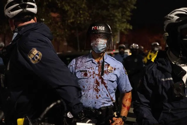 A riot police officer stands with a red smoothie splashed on him during clashes at a rally after the death of Walter Wallace Jr., a Black man who was shot by police in Philadelphia, Pennsylvania, October 27, 2020. Wallace, 27, was gunned down on October 26 by two police officers responding to what his relatives say was a call for assistance with a mental health crisis. (Photo by Yuki Iwamura/Reuters)