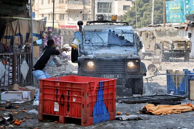 A Palestinian hurls a paint bucket at an Israeli military vehicle during a raid in Nablus in the Israeli-occupied West bank on February 22, 2023. (Photo by Raneen Sawafta/Reuters)