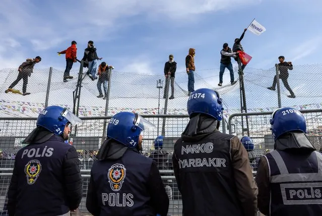 Police secure the stage as people stand on a fence during a gathering to celebrate Newroz, which marks the arrival of spring and the new year, in Diyarbakir, Turkey on March 21, 2023. (Photo by Umit Bektas/Reuters)