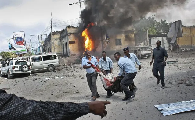 Somali security force members carry away a wounded civilian following a suicide car bomb blast in the capital Mogadishu, Somalia Sunday, May 5, 2013. A Somali police official at the scene said four civilians and a soldier were killed after the suicide bomber attempted to ram a car laden with explosives into a military convoy. (Photo by Farah Abdi Warsameh/AP Photo)