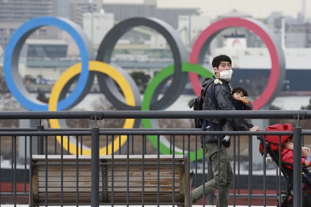 People wearing face masks to protect against the spread of the coronavirus walk on the Odaiba waterfront as Olympic rings is seen in the background in Tokyo, Tuesday, January 26, 2021. (Photo by Koji Sasahara/AP Photo)