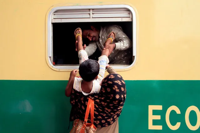 A man helps his wife to pull a child through a window of a train as they make their way home in Lahore, Pakistan on June 14, 2018. (Photo by Mohsin Raza/Reuters)