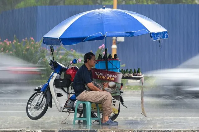 A vendor selling the popular Malay dish nasi lemak waits for customers next to his stall on the side of a road during a heavy rain downpour in Kuala Lumpur on April 4, 2023. (Photo by Mohd Rasfan/AFP Photo)