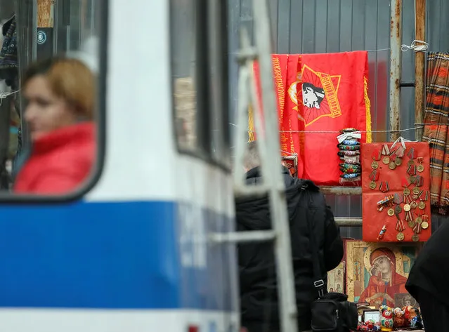 A woman sits in a trolleybus as a flag of the former Young Pioneer Organisation of USSR with a portrait of Lenin, icons and old soviet medals are on sale on the street in central Chisinau, Moldova, November 12, 2016. (Photo by Gleb Garanich/Reuters)