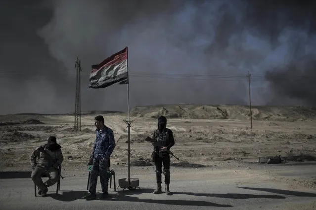 Guards stand at a checkpoint near burning oil fields in Qayara, south of Mosul, Iraq, Tuesday, November 22, 2016. For months, residents of the Iraqi town of Qayara have lived in the darkness from a cloud of toxic fumes released by oil fields lit by retreating Islamic State fighters. (Photo by Felipe Dana/AP Photo)