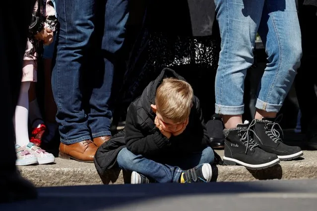 A child sits on the ground during a minute's silence outside Windsor Castle on the day of the funeral of Britain's Prince Philip, husband of Queen Elizabeth, who died at the age of 99, in Windsor, Britain, April 17, 2021. (Photo by Phil Noble/Reuters)