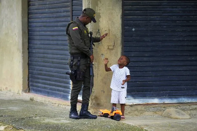 A police officer greets a toddler in a neighborhood that has criminal gangs in Buenaventura, Colombia, Thursday, August 17, 2023. (Photo by Fernando Vergara/AP Photo)