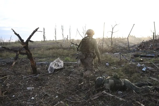 Assault unit commander from the 3rd Assault Brigade who goes by the call sign “Fedia”, passes by the body of a dead Russian soldier at the frontline in Andriivka, Donetsk region, Ukraine, Saturday, September 16, 2023. The 3rd Assault Brigade announced Friday they had recaptured the war-ravaged settlement which lies 10 kilometers (6 miles) south of Russian-occupied city of Bakhmut, in the country's embattled east. (Photo by Alex Babenko/AP Photo)