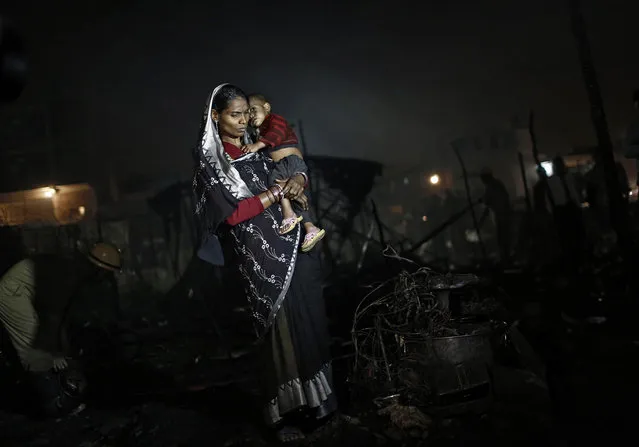 A slum dweller carries her child while standing next to her burnt belongings after a fire that broke out at a slum area in New Delhi November 11, 2013. Dozens of huts were gutted in the fire that broke out on Monday evening, with no causalities reported and the cause of the fire still unknown, firefighters said. (Photo by Adnan Abidi/Reuters)